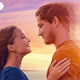 A couple standing on the beach, looking into each other's eyes.